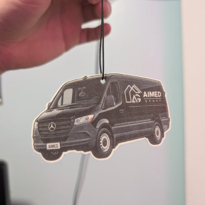 A finished black business van air freshener with its company branding, hanging from a black loop.