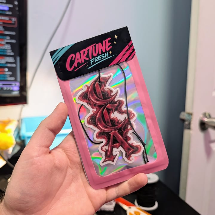 A red and black custom lettering air freshener in pink Cartune Fresh packaging with a holographic backing.