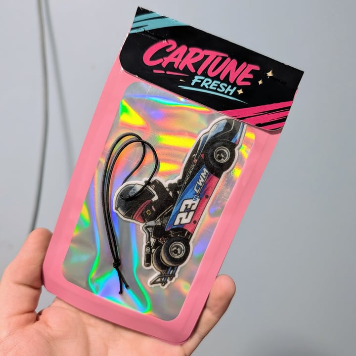 A finished black racing car air freshener in pink Cartune Fresh packaging, held against a plain light background.